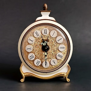 May include: White vintage alarm clock with gold accents and Roman numeral markings on the face. The clock has a decorative gold design on the face and a gold base.