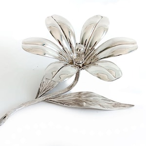 May include: A silver flower-shaped dish with five petals and a stem. The dish is made of metal and has a shiny finish.