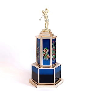 Op de afbeelding: Een gouden golf trofee met een blauwe en zwarte basis. De basis is versierd met een bloemenontwerp. De trofee staat op een witte achtergrond.