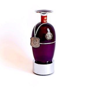 May include: A dark purple glass bottle with a silver cap and base. A silver chain with a decorative tag hangs from the neck. The bottle has a red label with the word "Scotch" on it. The bottle is on a white background.