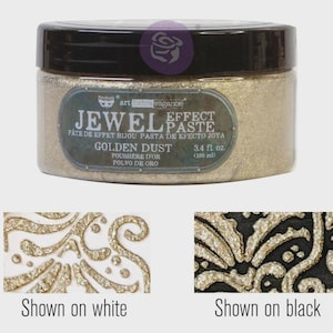Op de afbeelding: Een pot "Jewel Effect Paste" in de kleur "Golden Dust", met een zwart deksel. Het etiket geeft 100 ml aan. Twee voorbeelden tonen het effect van de pasta: één op wit en één op zwart, die de glittertextuur laten zien.