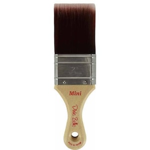 May include: A 2-inch (5 cm) Mini Dixie Belle paint brush with a light wood handle and dark brown bristles. The handle has the brand name and "Mini" printed in red. Made in USA is printed on the bottom of the handle.