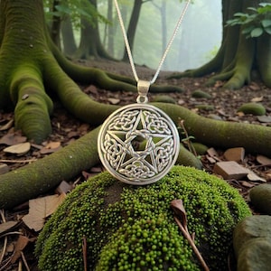 May include: A silver pendant necklace with a Celtic knot design encircling a five-pointed star. The pendant is suspended from a fine chain. The necklace is shown on green moss, with a forest backdrop.