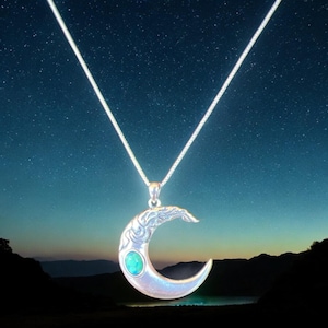 May include: A silver-toned crescent moon pendant necklace with an oval turquoise stone. The moon has an ornate design and hangs from a delicate silver chain. The background is a starry night sky.
