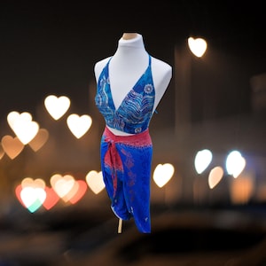 May include: A blue and pink halter top and wrap skirt set with a floral pattern. The set is on a white mannequin against a blurry background of heart-shaped lights.