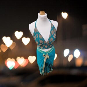 May include: A turquoise halter top with gold embroidery and a matching turquoise wrap skirt. The top has a deep V-neckline and the skirt is tied at the waist.