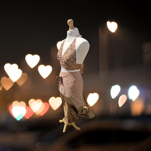 May include: A halter top and skirt set in a brown and white paisley print. The set is displayed on a mannequin against a blurred background of heart-shaped lights.