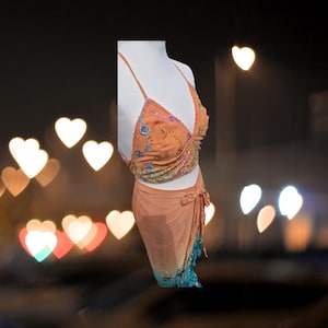 May include: A two-piece outfit with a peach-colored top and skirt. The top is a halter style with a V-neck and is decorated with colorful embroidery. The skirt is a wrap style with a tie at the waist and a gradient from peach to blue.