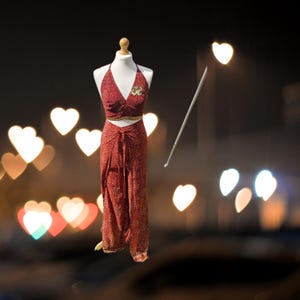 May include: A red halter top and matching wrap skirt with gold accents. The outfit is on a mannequin against a blurry background of heart-shaped lights.