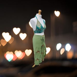 May include: A green wrap skirt with a floral print and a matching green halter top with a teal and white floral print. The outfit is displayed on a mannequin against a blurry background of heart-shaped lights.