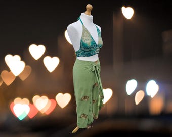 May include: A green wrap skirt with a floral print and a matching green halter top with a teal and white floral print. The outfit is displayed on a mannequin against a blurry background of heart-shaped lights.