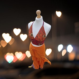 May include: A two-piece outfit with a halter top and a wrap skirt. The top is orange and red with sequins and beading. The skirt is orange and has a tie at the waist.