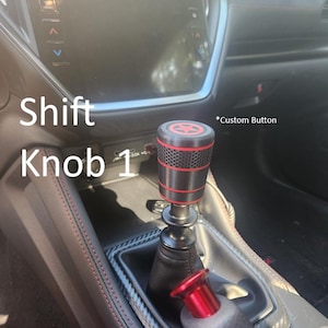 May include: A custom shift knob with a red and black design, featuring a star emblem. The image shows the knob installed in a car, with the text "Shift Knob 1" visible.
