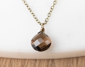 May include: A delicate gold chain necklace with a brown gemstone pendant. The pendant is faceted and has a teardrop shape.
