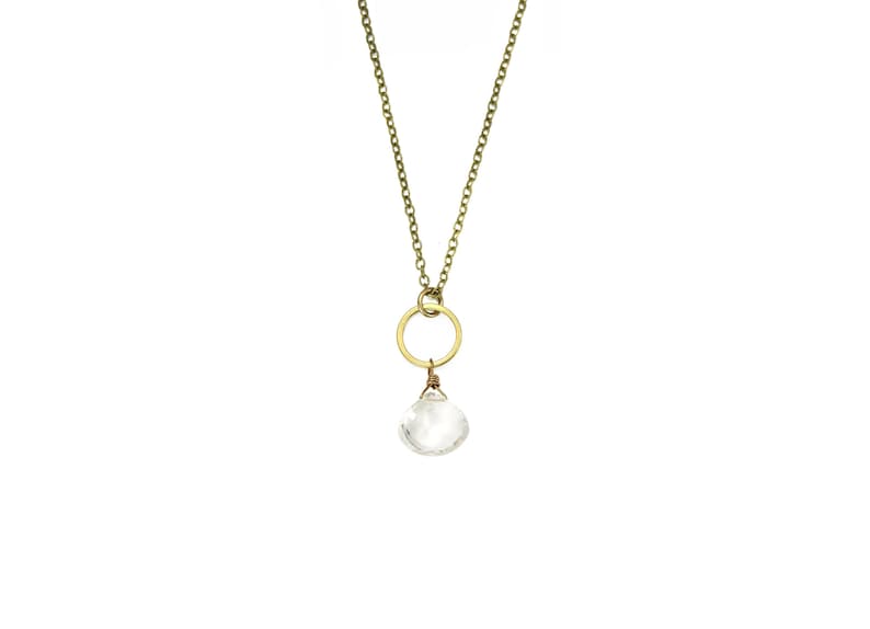 Op de afbeelding: Een gouden ketting met een kleine, heldere kristallen hanger en een gouden cirkelbedel.