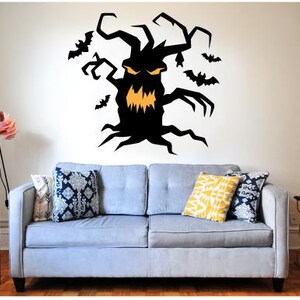 May include: A black Halloween tree wall decal with an orange face and bats. The spooky tree is mounted above a light blue sofa with decorative pillows. A floor lamp with a pink shade is to the left.