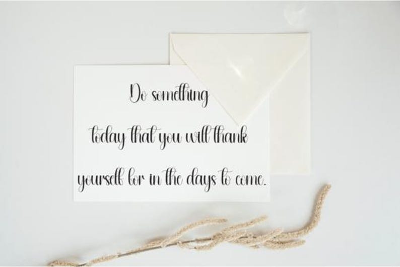 May include: A white card with the handwritten text "Do something today that you will thank yourself for in the days to come." An envelope and dried plant sprig are also present.