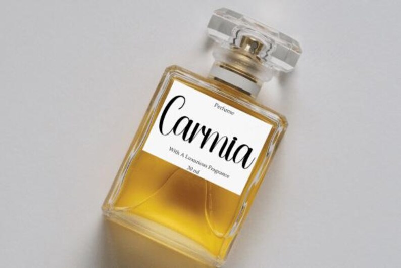 May include: A rectangular perfume bottle with a clear, faceted cap and a gold-coloured neck. The bottle contains a golden liquid and has a white label with the word "Carnia" in cursive. The label also includes the text "Perfume" and "With A Luxurious Fragrance 30 ml."