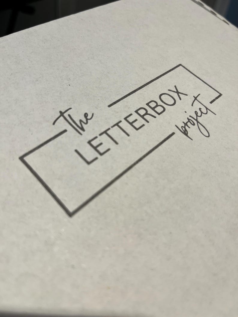 Pu&ograve; includere: Una scatola bianca con il testo "The Letterbox Project" in una cornice quadrata nera.