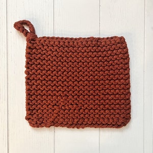 May include: A rust-coloured knitted pot holder with a loop handle.