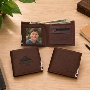 May include: Three brown leather wallets. One is open, showing a photo of a young person, a zippered pocket, and text reading Custom Your Text Here. The other two are closed, one featuring a mountain graphic with the text Adventure Awaits James.