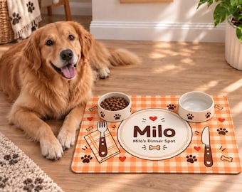 Puede incluir: Un tapete de alimentación rectangular para mascotas con cuadros naranjas y blancos, que presenta un diseño circular central con el texto "Milo" y "Milo's Dinner Spot", junto a ilustraciones de un tenedor, cuchillo, huellas, corazones y huesos.