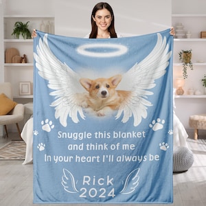 May include: A light blue blanket featuring a corgi with angel wings and a halo. The blanket has the text "Snuggle this blanket and think of me, In your heart I'll always be, Rick 2024" and paw prints.