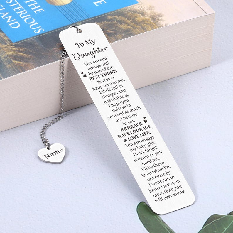 May include: Silver bookmark with a heart-shaped charm and a message for a daughter. The bookmark reads "To My Daughter You are and always will be one of the BEST THINGS that ever happened to me. Life is full of changes and possibilities, I hope you believe in yourself as much as I believe in you. BE BRAVE, HAVE COURAGE & LOVE LIFE. You are always my baby girl. Don't forget whenever you need me, I'll be there. Even when I'm not close by I want you to know I love you more than you will ever know."