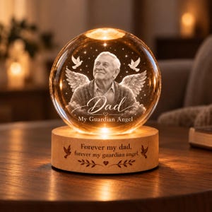 May include: A spherical glass ornament featuring an etched portrait of a man with angel wings, the text "Dad My Guardian Angel," and a wooden base engraved with "Forever my dad, forever my guardian angel" and two small bird icons.
