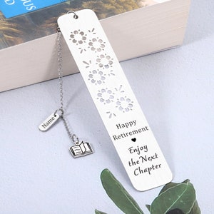 Puede incluir: Marcap&aacute;ginas de plata con un dise&ntilde;o recortado de fuegos artificiales y el texto "Happy Retirement Enjoy the Next Chapter". El marcap&aacute;ginas tiene un peque&ntilde;o amuleto de plata unido a una cadena que dice "Name" y un peque&ntilde;o amuleto de plata de un libro abierto.
