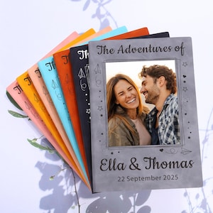 May include: A grey photo album with a photo of a couple in a frame. The album has the text "The Adventures of Ella & Thomas 22 September 2025" printed on the front.