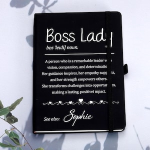May include: Black notebook with the text "Boss Lady" in white, along with a definition. The notebook has an elastic band closure and a decorative heart design. The name "Sophie" is also included.