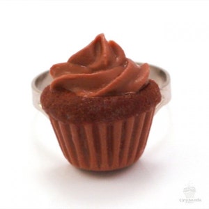 Könnte beinhalten: Ein Schokoladen-Cupcake-Ring mit braunem Frosting. Der Ring ist aus Metall und hat einen braunen Cupcake-Anhänger.