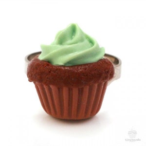 Könnte beinhalten: Ein grüner und brauner Cupcake-Ring. Der Cupcake ist aus Polymer Clay gefertigt und hat einen grünen Frosting-Wirbel auf der Oberseite. Der Ring ist aus Silbermetall.