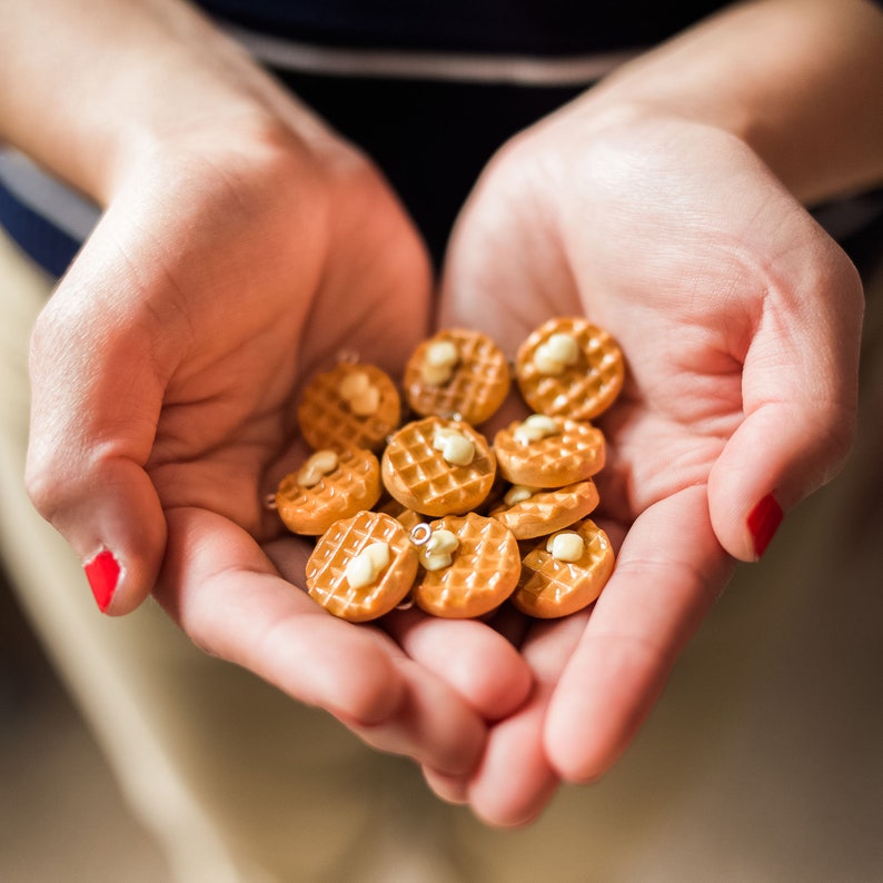 Op de afbeelding: Een verzameling kleine, bruine, wafelvormige oorbellen met witte centra. De oorbellen worden in de handpalmen van een persoon gehouden.
