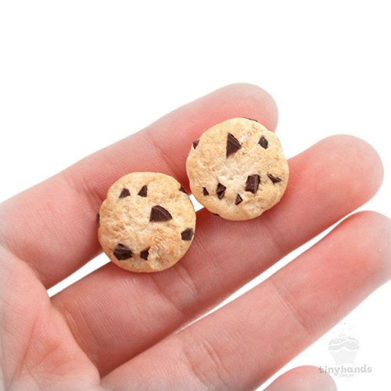 May include: A pair of chocolate chip cookie earrings. The cookies are brown and have chocolate chips on top.