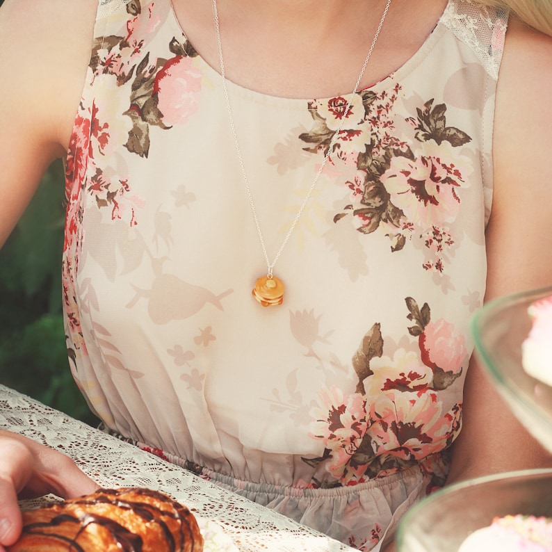 May include: A woman wearing a floral print dress with a gold necklace featuring a stacked pancake charm.