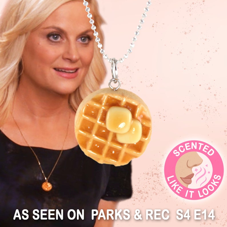 Op de afbeelding: Een zilveren ketting met een hanger in de vorm van een wafel. De hanger is gemaakt van bruin en geel polymer clay en heeft twee kleine gele vierkantjes bovenop, die op boter lijken. De hanger is versierd met een wafelpatroon. De ketting heeft een roze achtergrond met de tekst "SCENTED LIKE IT LOOKS" in een witte cirkel.