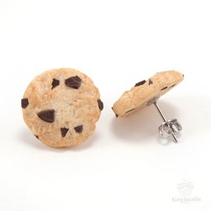 May include: A pair of chocolate chip cookie earrings. The earrings are made of polymer clay and are shaped like chocolate chip cookies. The earrings are on a silver post.