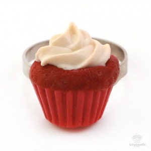 Könnte beinhalten: Ring in Form eines roten Samt-Cupcakes mit weißem Frosting. Der Cupcake ist aus Polymer Clay gefertigt und eine realistische Nachbildung eines echten Cupcakes.