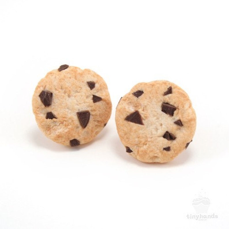 May include: A pair of chocolate chip cookie earrings. The earrings are made of polymer clay and are shaped like chocolate chip cookies. The cookies are brown with chocolate chips.
