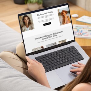 K&ouml;nnte beinhalten: Eine Person benutzt einen silbernen Laptop, auf dem eine Website mit dem Text "Hi, I'm [Your Name]" und "Here's How I Empower Businesses to Achieve Their Goals:" angezeigt wird. Der Laptop befindet sich auf dem Scho&szlig; einer Person, die Tastatur ist sichtbar.