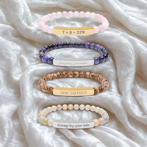May include: Four stretch bracelets featuring round beads and a central metal bar. The top bracelet has light pink beads and a gold bar with T + B ♥ 279. The second has purple beads and a silver bar with yes girl, you can. The third has brown speckled beads and a gold bar with GROW THROUGH IT. The bottom has beige beads and a silver bar with Always by your side.