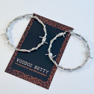 May include: A pair of silver hoop earrings made of barbed wire. The earrings are large and have a punk rock aesthetic.