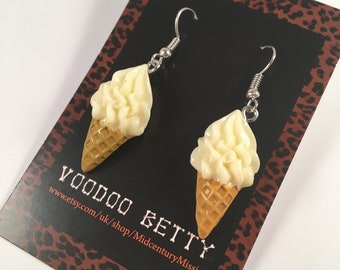 May include: A pair of dangle earrings featuring a white ice cream cone with a waffle cone. The earrings are on a card with the text "Voodoo Betty www.etsy.com/uk/shop/MidcenturyMissie".