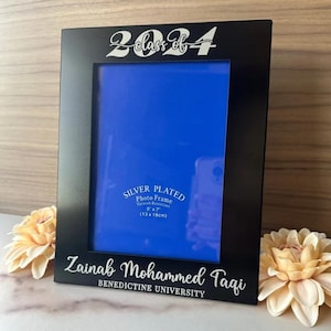 May include: Black picture frame with a silver plated finish. The frame has a 5x7 inch opening and says "Class of 2024" at the top. The bottom of the frame says "Zainab Mohammed Tagi, Benedictine University".