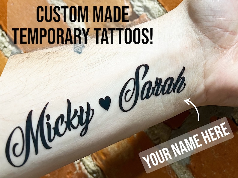 Pu&ograve; includere: Tatuaggi temporanei personalizzati con i nomi "Micky" e "Sarah" sul braccio di una persona. Il testo "YOUR NAME HERE" &egrave; anche visibile.