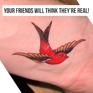 Pu&ograve; includere: Un tatuaggio temporaneo di una rondine rossa e nera in volo. Il tatuaggio &egrave; sul braccio di una persona. Il testo "YOUR FRIENDS WILL THINK THEY'RE REAL!" &egrave; sopra il tatuaggio.