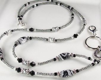 May include: A beaded lanyard with a silver clasp and key ring. The lanyard features small silver beads, black and white patterned beads, black faceted beads, and pearl-like beads. The lanyard is designed to hold keys or an ID badge.