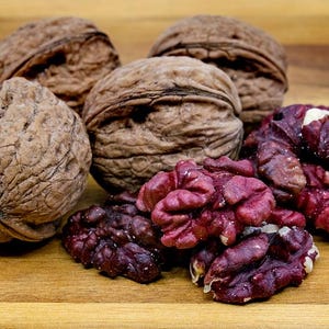 Puede incluir: Un grupo de nueces, algunas con sus cáscaras quitadas, revelando la pulpa de color púrpura oscuro en el interior. Las nueces están sobre una superficie de madera.